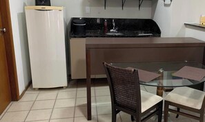 A compact kitchen with a refrigerator, stove, and a glass dining table with chairs.