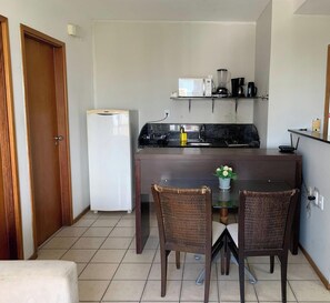 A compact kitchen with a refrigerator, microwave, coffee maker, and a small dining table with chairs.
