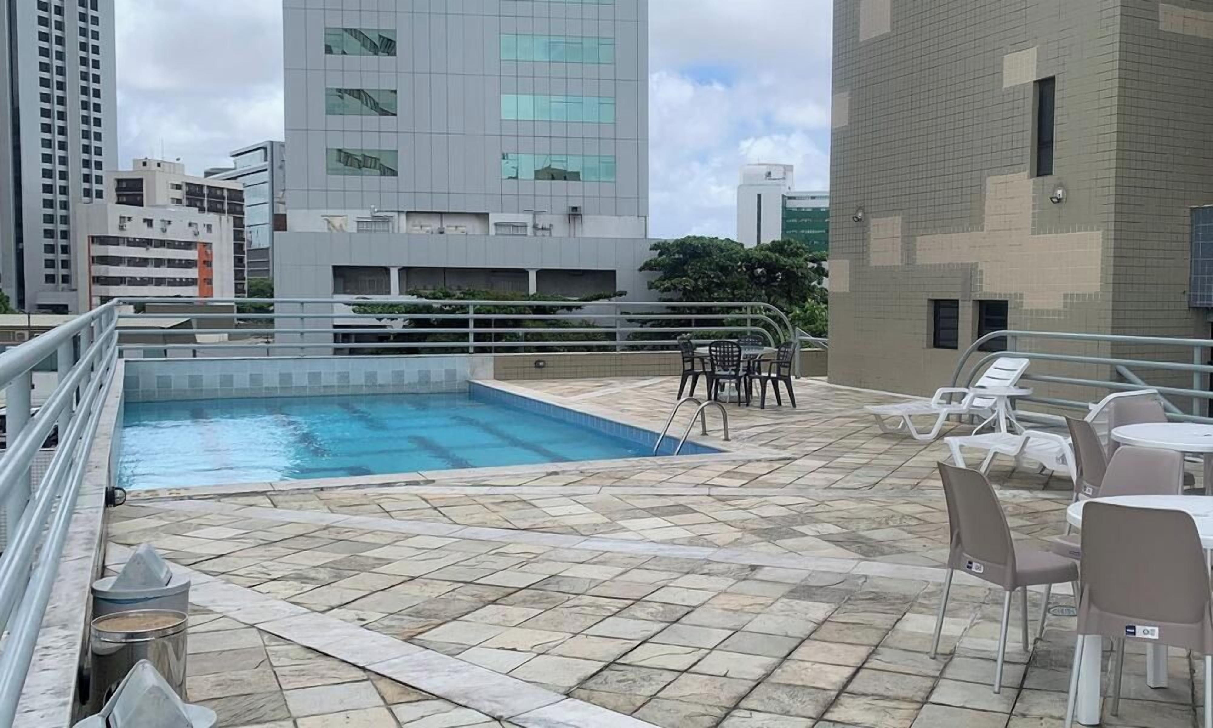 A rooftop pool area with a swimming pool, chairs, and tables.