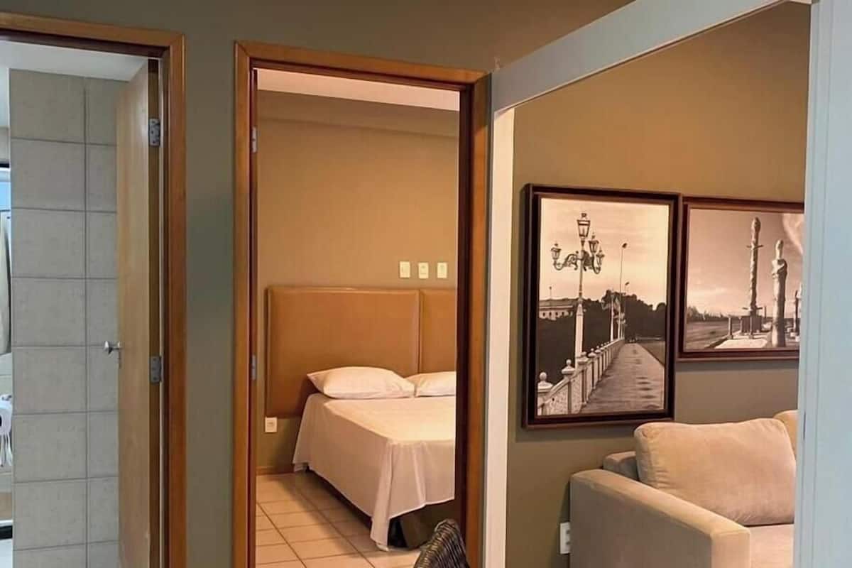 A hotel room with a bed, a chair, and two framed pictures on the wall.