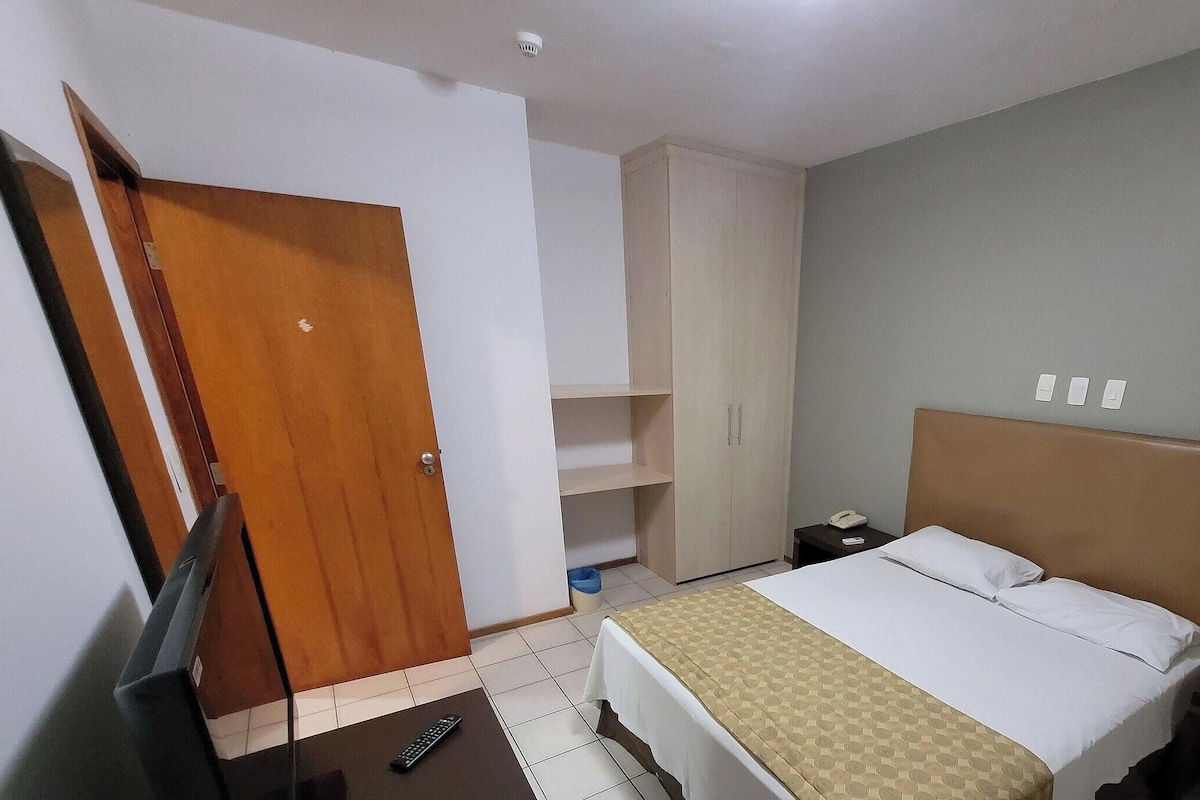 A bedroom with a bed, a wardrobe, a nightstand, a telephone, and a television.