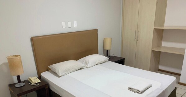 A hotel room with a bed, bedside lamp, phone, and a wardrobe.