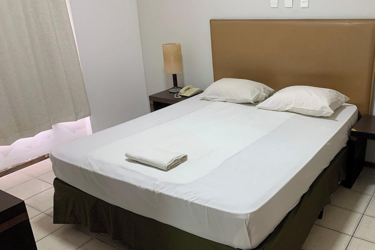 A hotel room with a bed, a nightstand, a lamp, and a telephone.