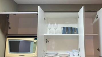 A kitchen with a microwave, a cabinet with dishes and glasses, and a power outlet.