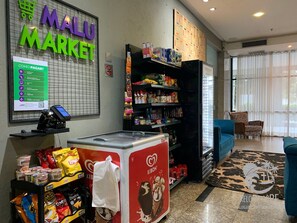 A market area with a self-service kiosk, shelves stocked with snacks, and a sign for MALU MARKET.