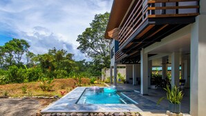 A modern outdoor pool area with a clear view of the surrounding landscape, including trees and a building with a balcony. - 3-bedroom villa in Platanillo, ocean & mountain view! (Platanillo)
