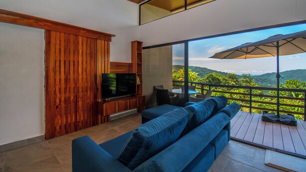A modern living room with a large TV, blue sofas, and a wooden entertainment unit. - 3-bedroom villa in Platanillo, ocean & mountain view! (Platanillo)