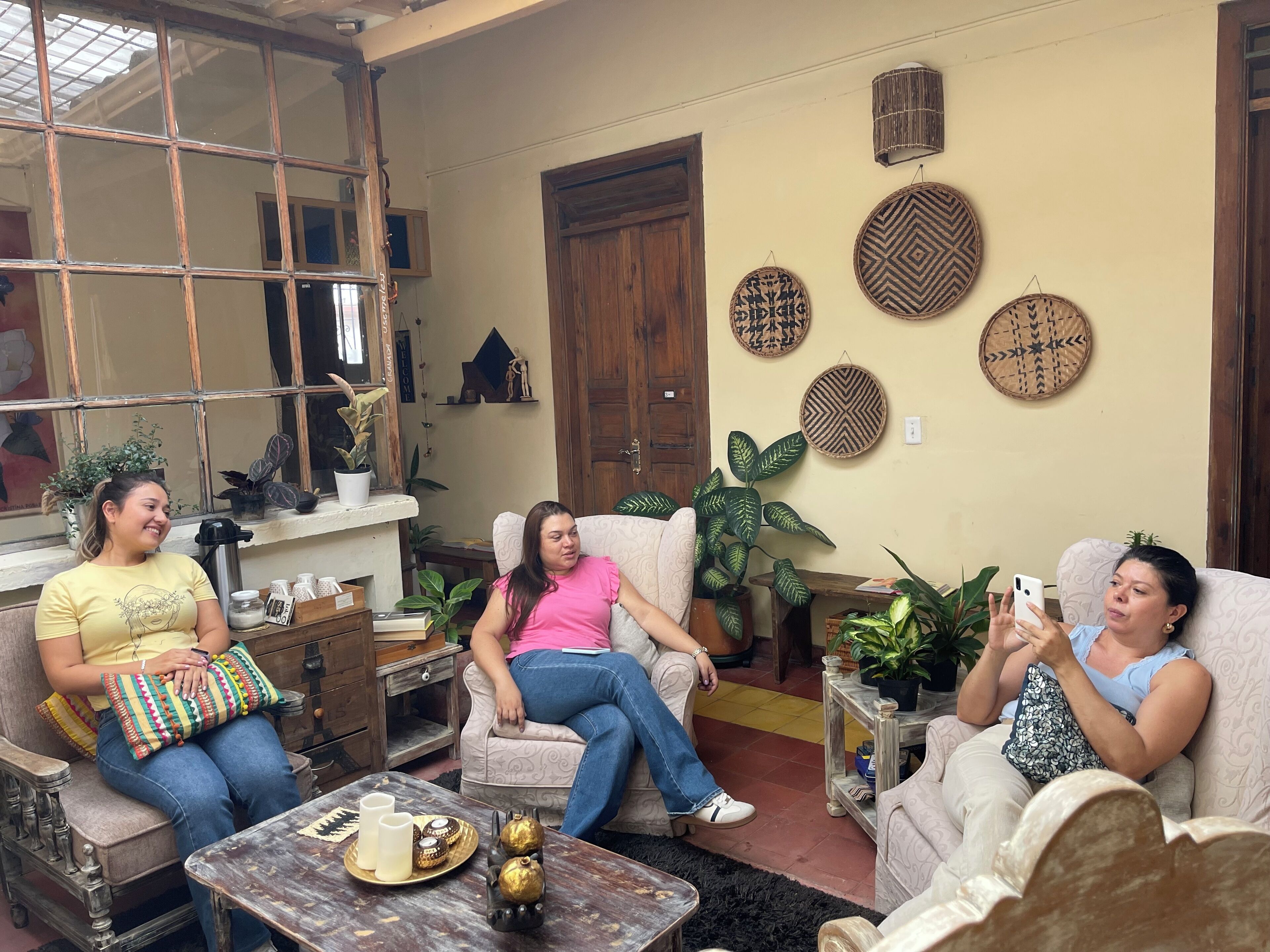 Un salon chaleureux où trois personnes sont assises sur des canapés, avec une table basse agrémentée d’objets décoratifs et divers éléments décoratifs fixés aux murs.