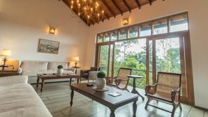 Habitación amplia con una cama grande, un sofá, una mesa de centro y dos sillas. Amplias ventanas ofrecen vistas a zonas verdes.
