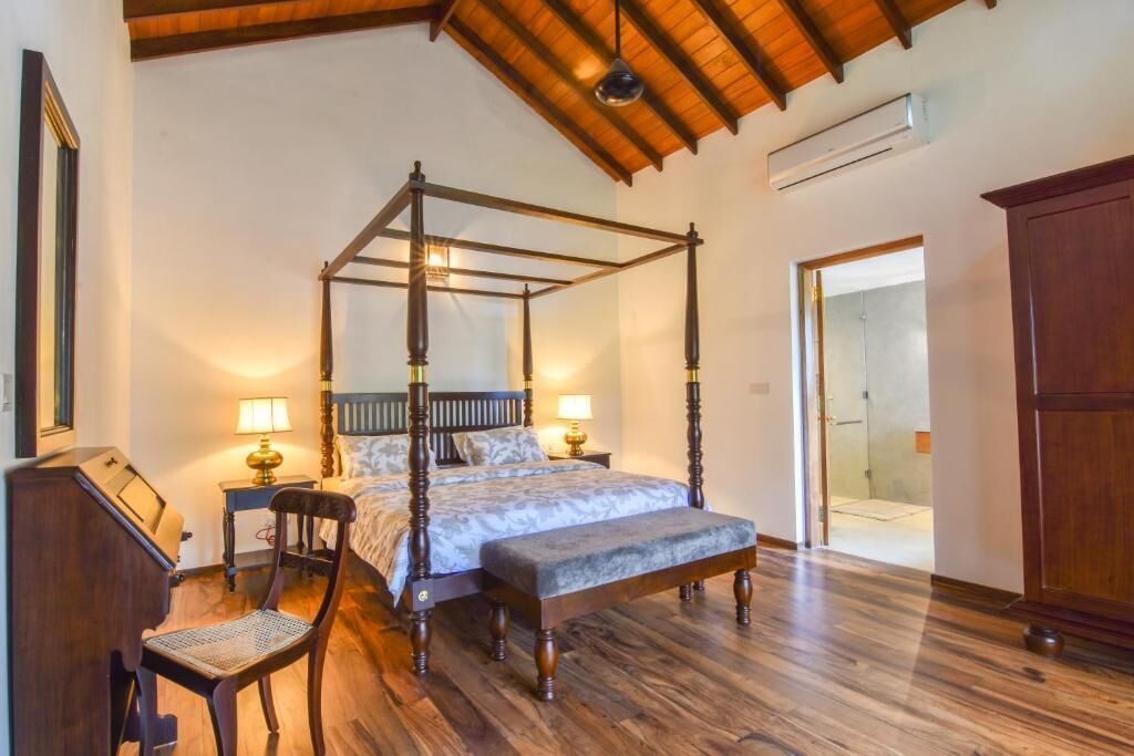A four-poster bed with a wooden frame and a bench at the foot, a desk with a chair, and a wardrobe.