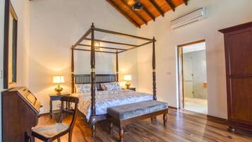 A four-poster bed with a wooden frame and a bench at the foot, a desk with a chair, and a wardrobe.