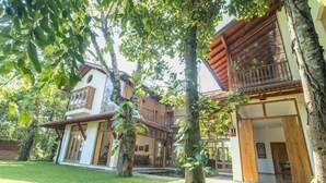 Una casa de dos pisos con un balcón, rodeada de árboles y un césped cuidado.