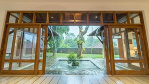 Puerta de cristal con marco de madera que da a un jardín con una pequeña fuente y un árbol.