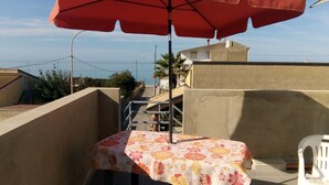Ein Patio mit Tisch, bedeckt mit einer blumigen Tischdecke und einem roten Sonnenschirm.