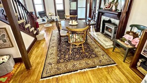 A spacious living room with a wooden floor, a dining table with chairs, a fireplace, and a staircase leading to another level. - The Pearl - Waterfront Retreat  • 4BR • 7 Bed • Family / Friends / Pets (Colonial Beach)