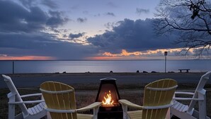 Two Adirondack chairs facing a fire pit with a view of a sunset over a body of water. - The Pearl - Waterfront Retreat  • 4BR • 7 Bed • Family / Friends / Pets (Colonial Beach)
