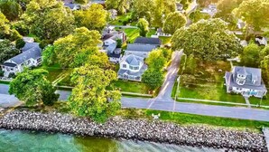 An aerial view of a residential area with houses, a road, and a stone seawall. - The Pearl - Waterfront Retreat  • 4BR • 7 Bed • Family / Friends / Pets (Colonial Beach)