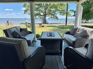Um alpendre coberto com móveis de vime, uma mesa e vista para o mar.