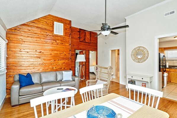 A living room with a wooden wall, a sofa, a dining table, and a ceiling fan. - 900. B Seaside 2 Br Cottage with Bay Views, Veranda, High Ceilings, Hot Tub, Private Beach, Beachfront Grilling, & Kayaks (Norfolk)