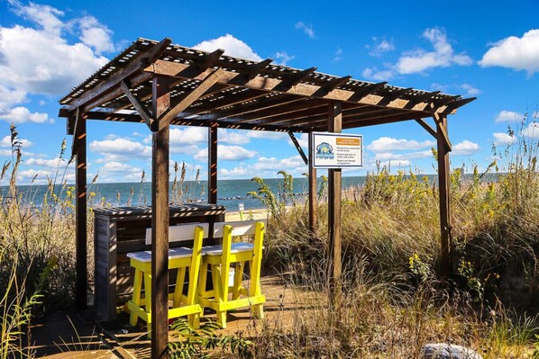 Un mirador de madera con una mesa y sillas amarillas, con vista a una playa y el océano al fondo.