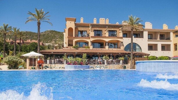 A hotel with a pool area, palm trees, and a mountainous backdrop. - Holiday Village Bonavista de Bonmont (Mont-roig del Camp)