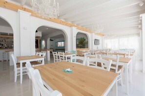Un comedor amplio con mesas y sillas blancas, vigas de madera y una araña.