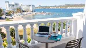 A balcony with a laptop, a cup of coffee, and a pair of glasses on a table, overlooking a coastal area with boats and a hotel in the background. - Beach Star Ibiza Hotel (Sant Josep de sa Talaia)