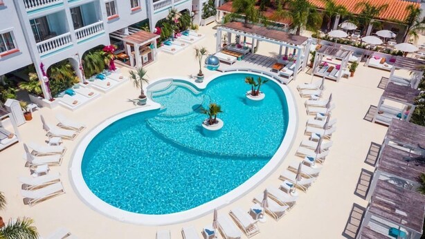 A heart-shaped pool surrounded by lounge chairs and umbrellas, with a building in the background. - Beach Star Ibiza Hotel (Sant Josep de sa Talaia)