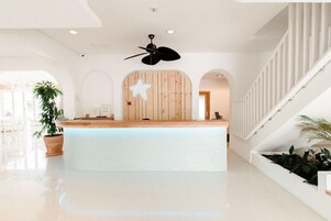 Un área de recepción con una decoración de estrella de madera, un ventilador de techo y una escalera con barandales blancos.