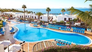 Un resort con una piscina grande, tumbonas y palmeras.