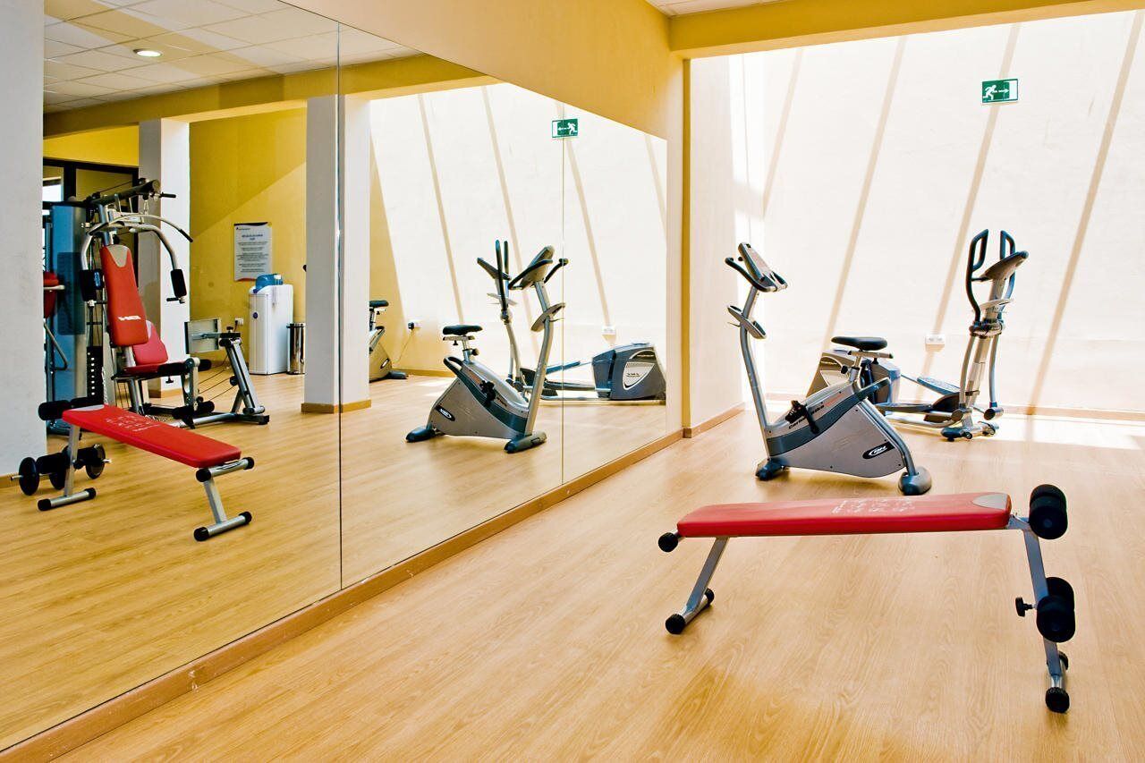 A gym with exercise equipment, a mirror, and a wooden floor.