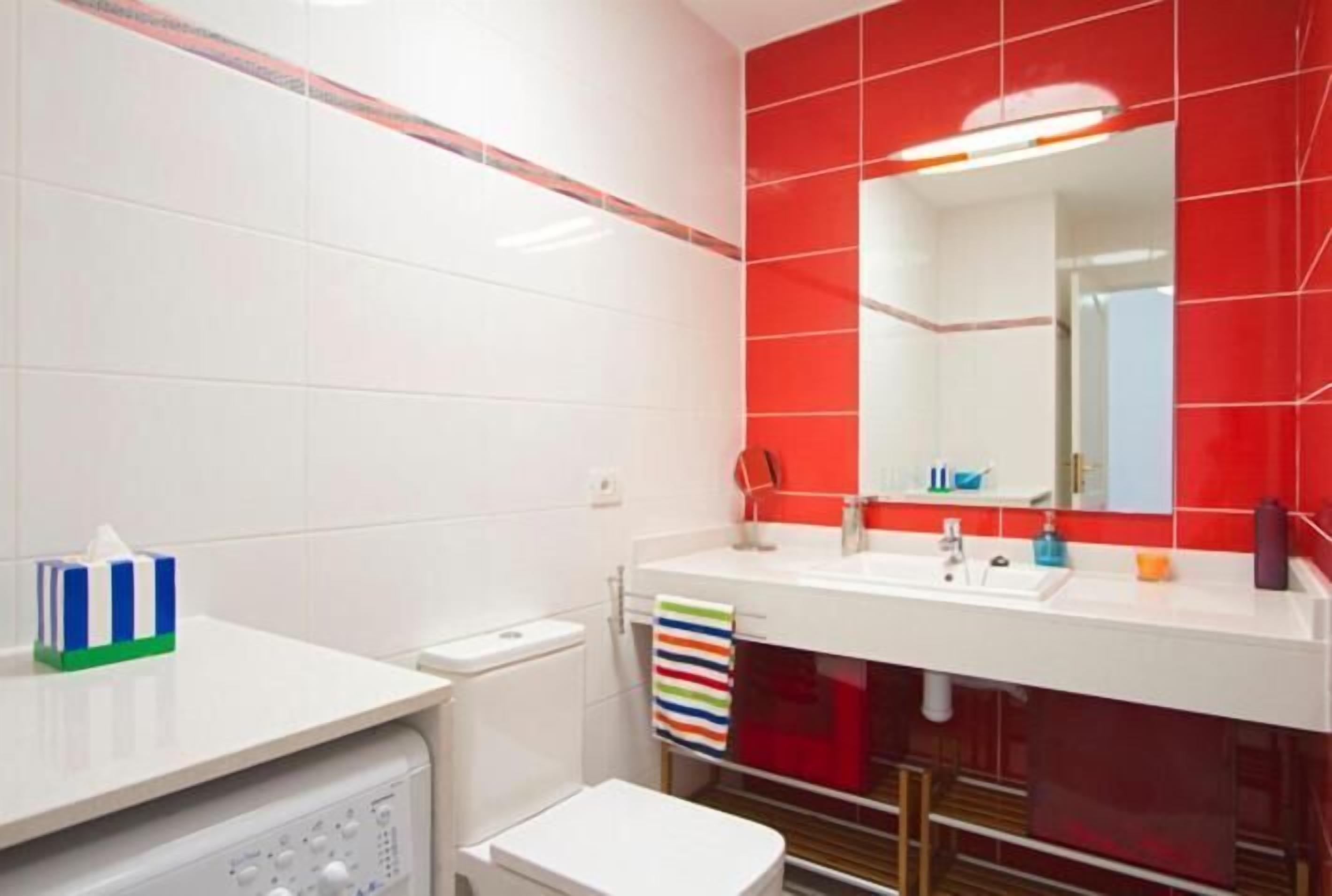 Een badkamer met witte tegels, een accentmuur met rode tegels, een witte wastafel, een spiegel en een toilet.