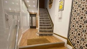 A staircase with wooden steps and a glass railing, leading to a room with patterned walls and a door.