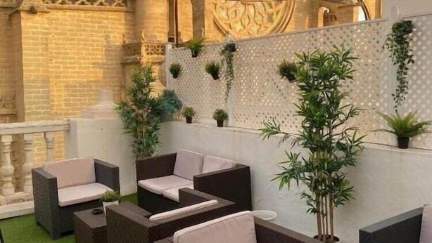 A rooftop patio with wicker furniture and potted plants, overlooking a historic building with intricate architecture.