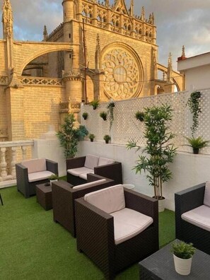 A rooftop patio with wicker furniture and potted plants, overlooking a historic building with intricate architecture. - Leonardo Da Vinci (Seville)