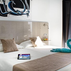 Moderni hotellihuone, jossa on sänky, tyynyjä, tabletti ja pyyhe.