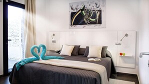 A modern hotel room with a large bed, two bedside tables, a wall-mounted artwork, and a view through a window with a curtain. - FBC Fortuny Resort - Adults Only (San Bartolomé de Tirajana)