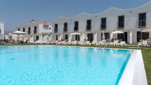 A swimming pool with sun loungers and umbrellas, surrounded by white buildings with balconies. - FBC Fortuny Resort - Adults Only (San Bartolomé de Tirajana)