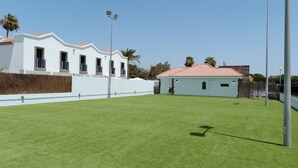 A modern building with a white facade and red-tiled roof, surrounded by a well-maintained lawn and palm trees. - FBC Fortuny Resort - Adults Only (San Bartolomé de Tirajana)