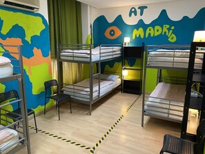 A bunk bed room with a world map mural, a chair, and a bed with a lamp. - Hostel Era (Madrid)