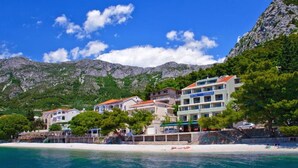 Un hôtel situé sur la côte, composé de plusieurs bâtiments, avec une plage et des montagnes en arrière-plan.
