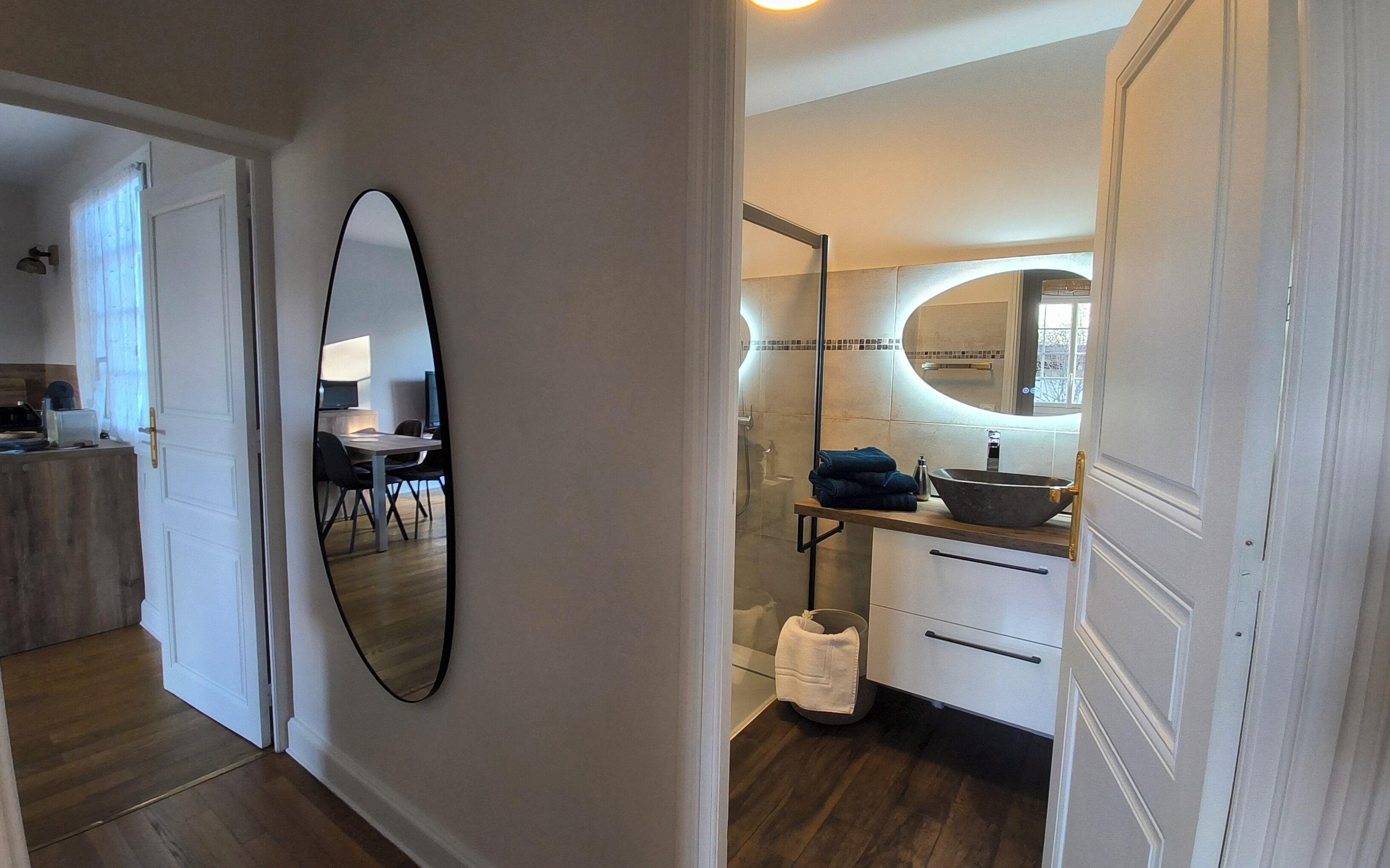 Un couloir avec un grand miroir, une petite table avec un ordinateur portable et une salle de bain avec un lavabo et un miroir.