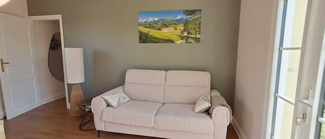 A room with a beige sofa, a door, a wall-mounted picture, and a window.