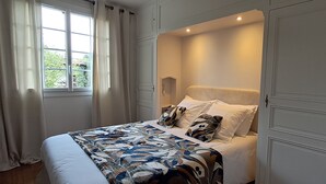 Une chambre avec un grand lit, des rideaux blancs, une fenêtre et une porte.