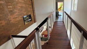 Eine Holztreppe mit weißen Geländern führt zu einem Balkon mit Ausblick ins Freie.
