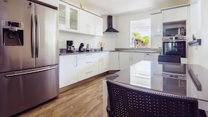 A modern kitchen with stainless steel appliances, white cabinetry, and a glass-top dining table. - Very nice spacious apartment with Jacuzzi - Le Canopé (Le Gosier)