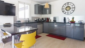 A modern kitchen with grey cabinets, a black countertop, and a yellow chair. - Modern villa with pool in a natural setting (Les Abymes)