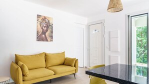 A modern living space with a yellow sofa, a dining table with yellow chairs, and a large window offering a view of greenery. - Modern villa with pool in a natural setting (Les Abymes)