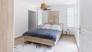 A bedroom with a wooden bed, a hanging light, a small side table, and a window with blinds. - Modern villa with pool in a natural setting (Les Abymes)