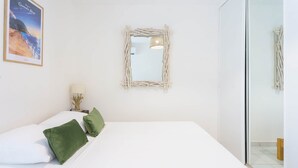 Ein Schlafzimmer mit einem Bett, Kissen, einem Spiegel, einem Wandbild und einer Nachttischlampe.